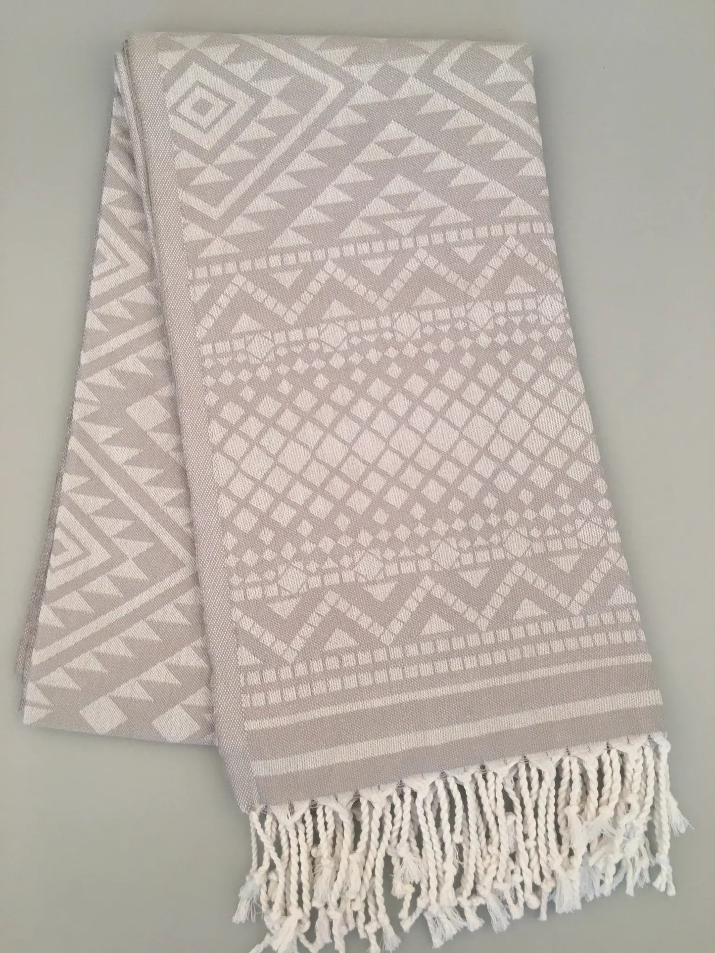 "Light gray Turkish towel with jacquard patterns in white, featuring fringed edges, folded view."