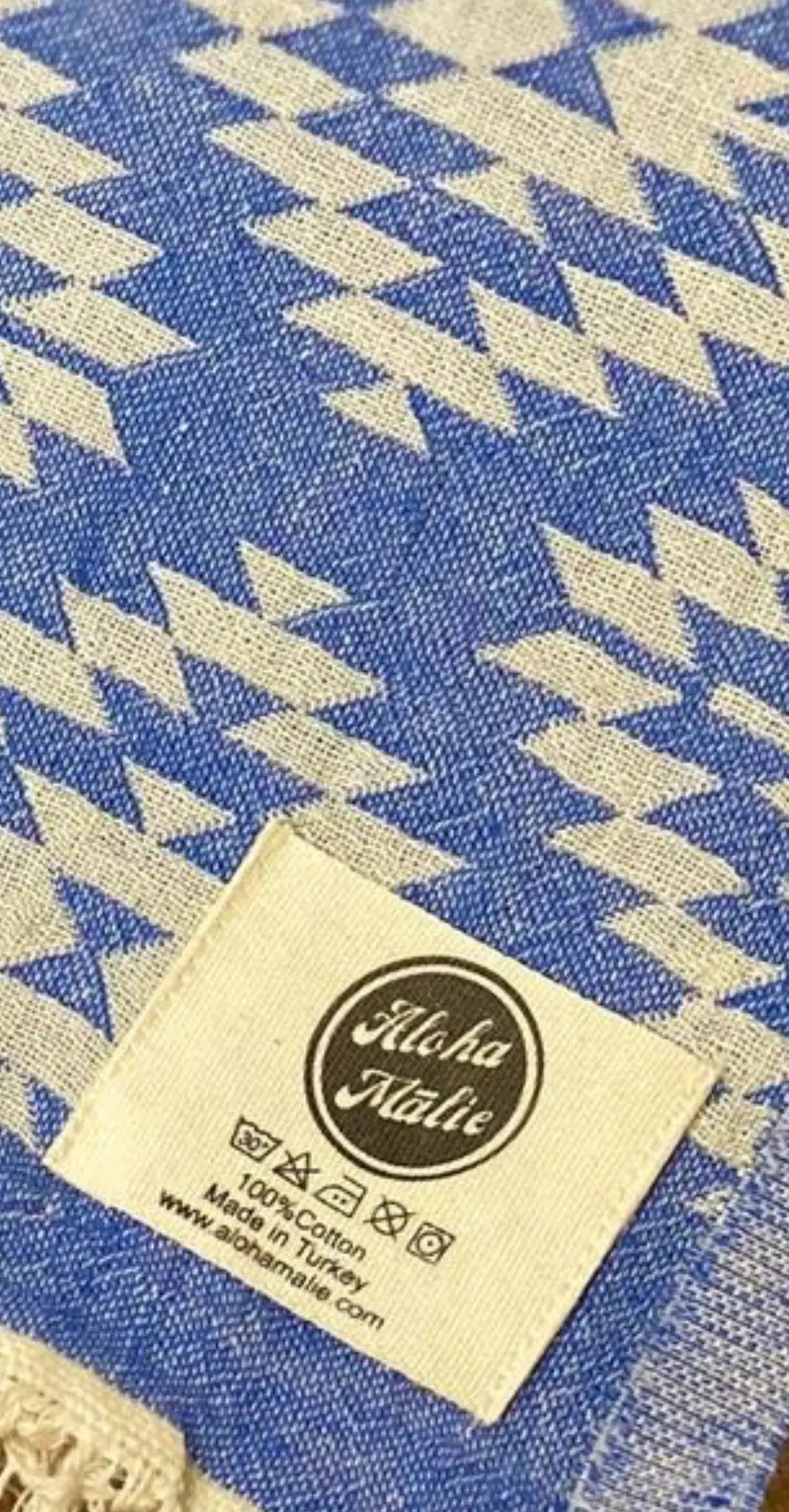 "Blue cotton label with zigzag pattern and cream background, featuring a white tag with black text at the bottom."