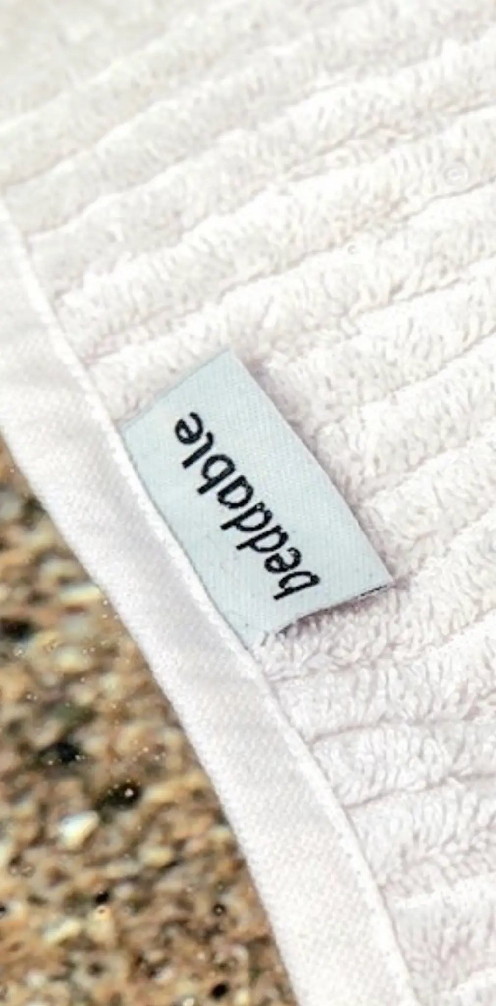 White cotton label with textured surface, featuring the word "beaddable" in black text, positioned on a light fabric.