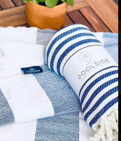 "White and blue striped cotton label with tassels, resting on a textured light blue and white blanket."