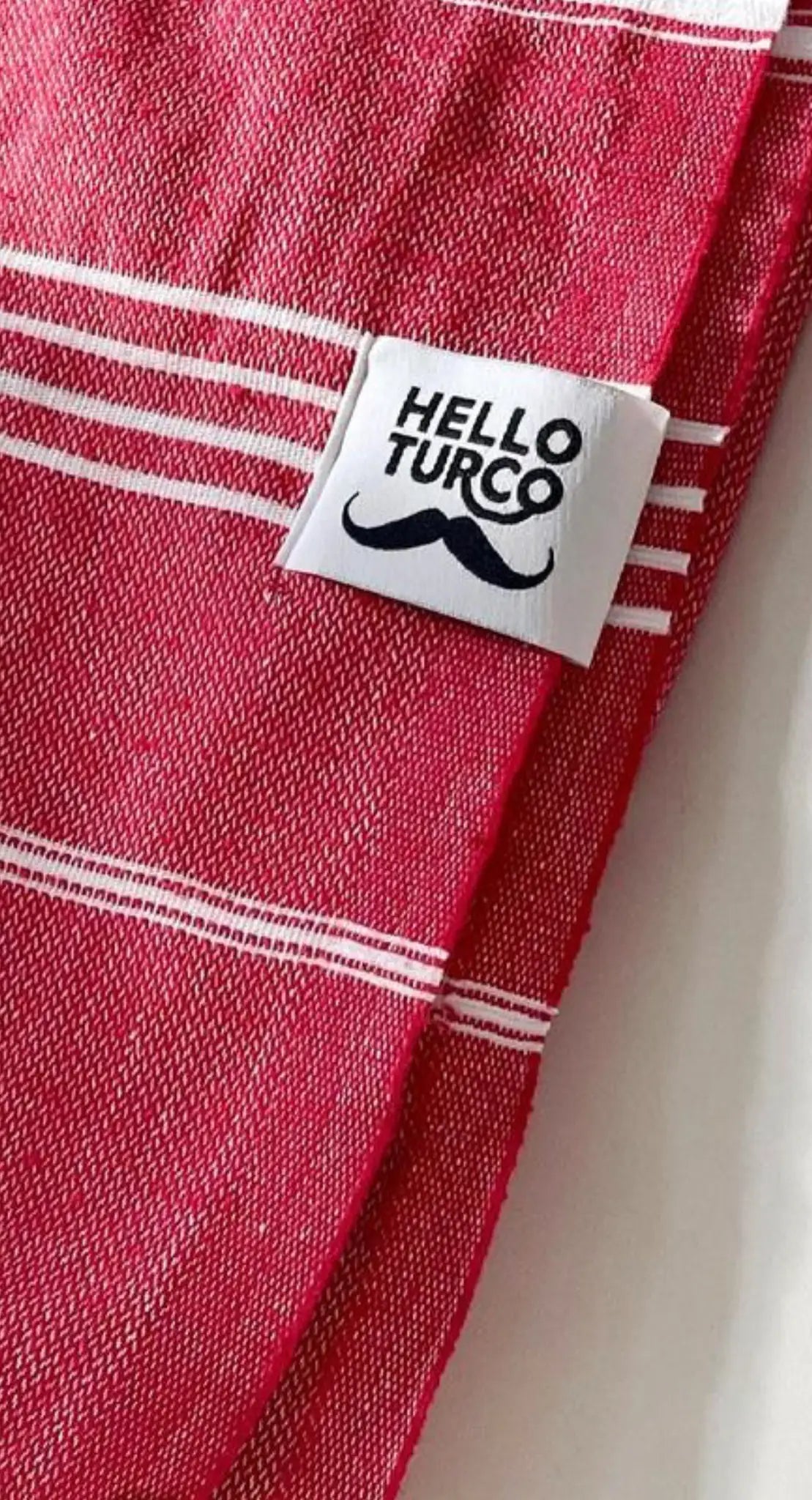 Red cotton label with white stripes, featuring a printed "HELLO TURCO" logo and a mustache design, side view.