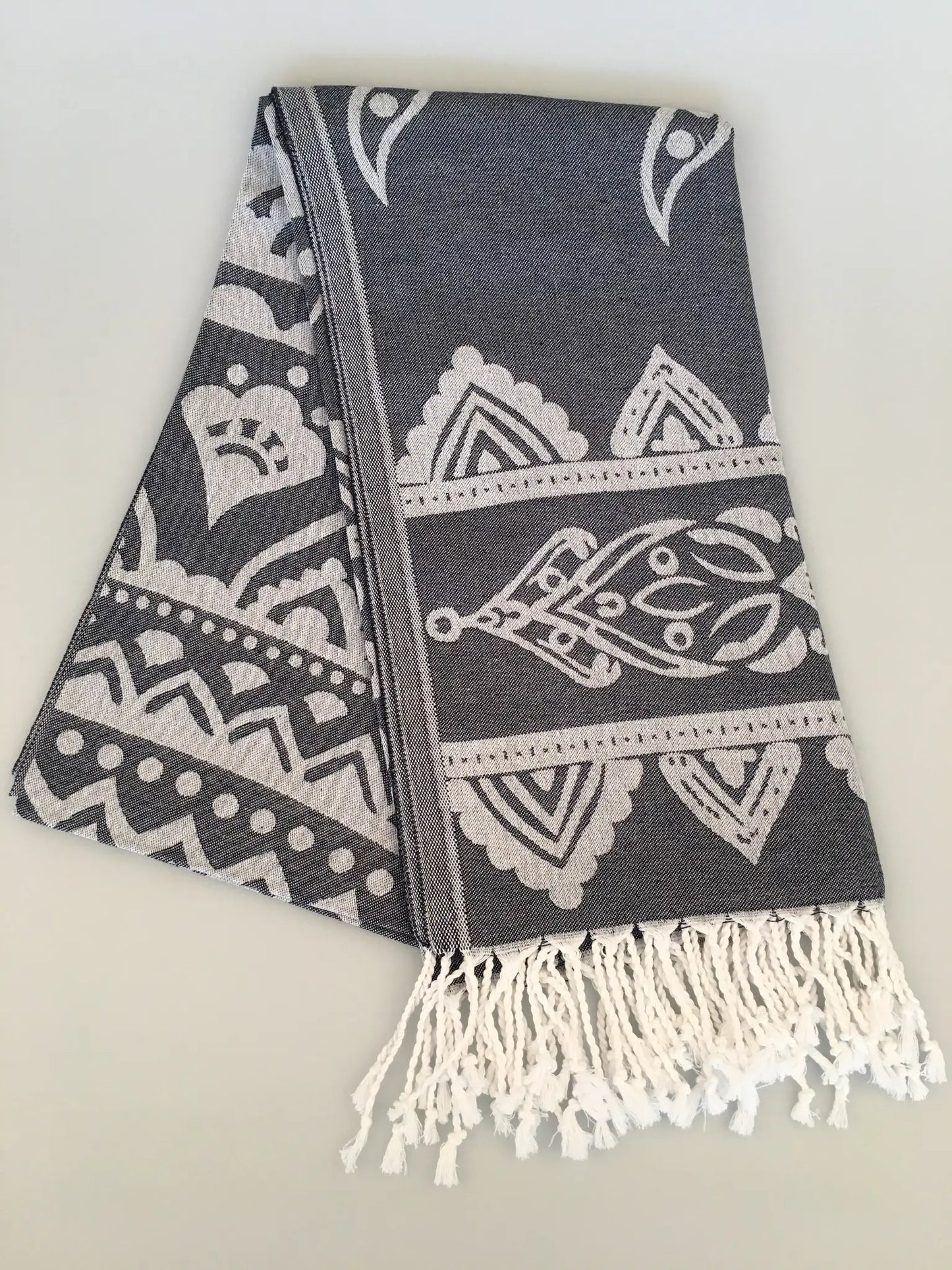 "Gray jacquard peshtemal towel with white intricate patterns and fringed edges, folded view on a light background."