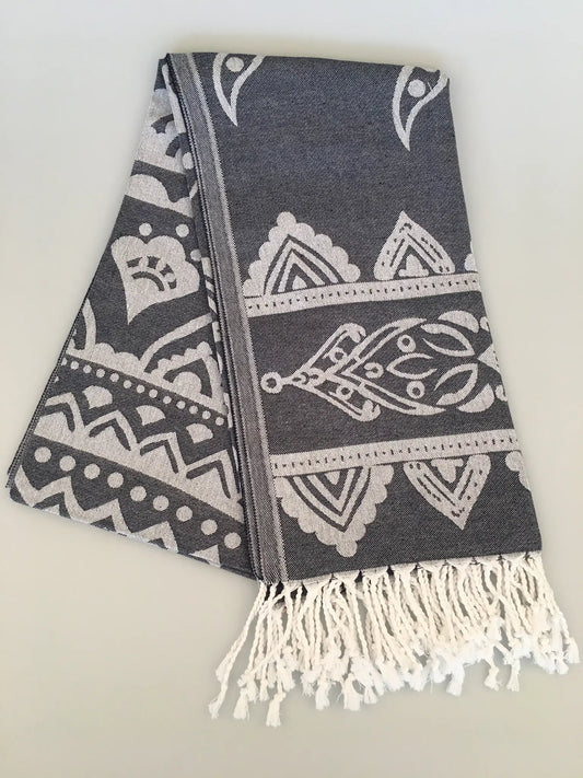 "Gray jacquard peshtemal towel with white intricate patterns and fringed edges, folded view on a light background."