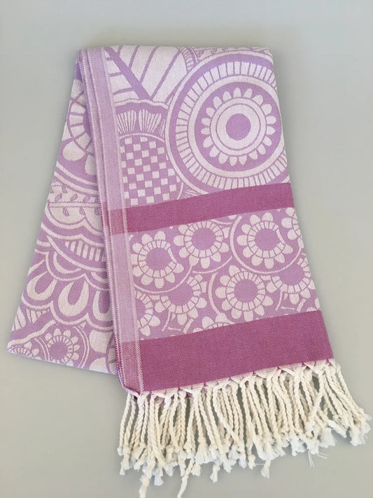 "Jacquard peshtemal towel in light purple with intricate circular patterns and white fringes, folded on a light surface."