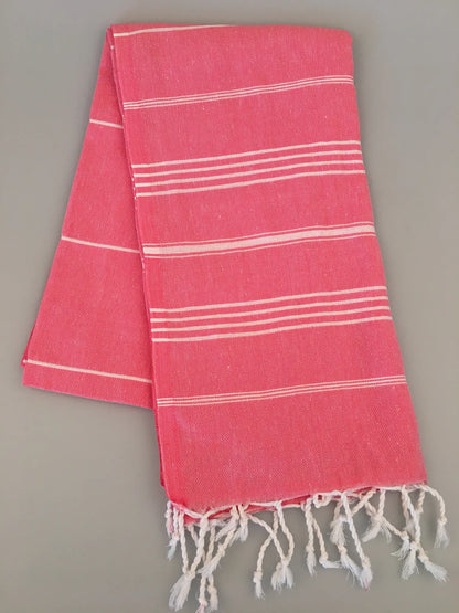 Coral pink Turkish towel with white stripes, fringed edges, and a lightweight, textured weave, laid flat.