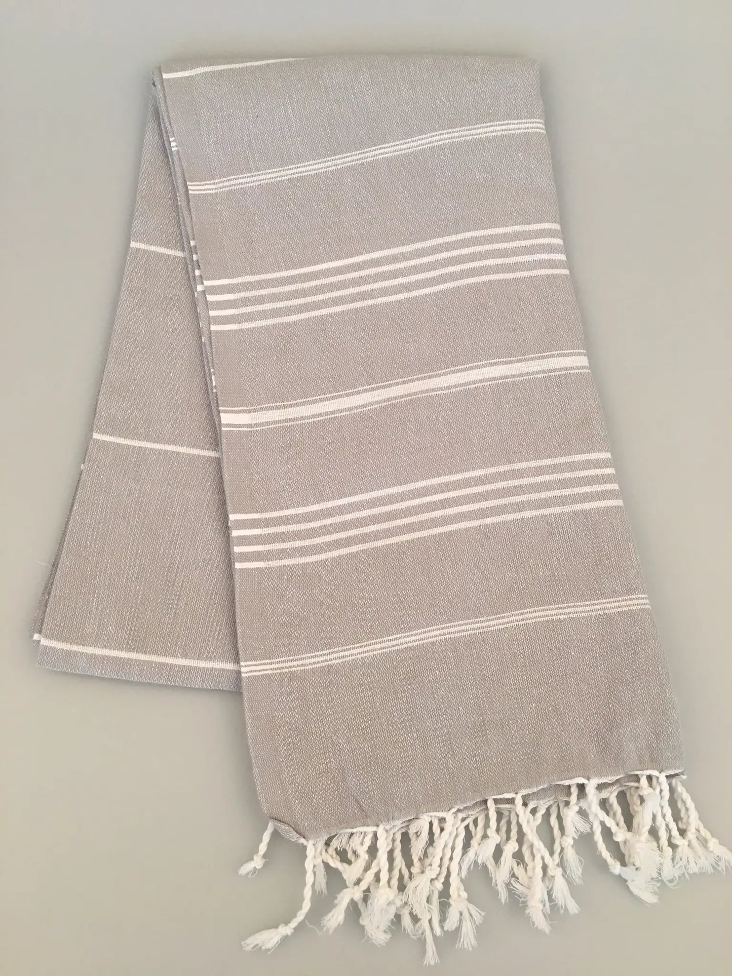 "Gray Turkish towel with white stripes and fringed edges, folded neatly on a light background."