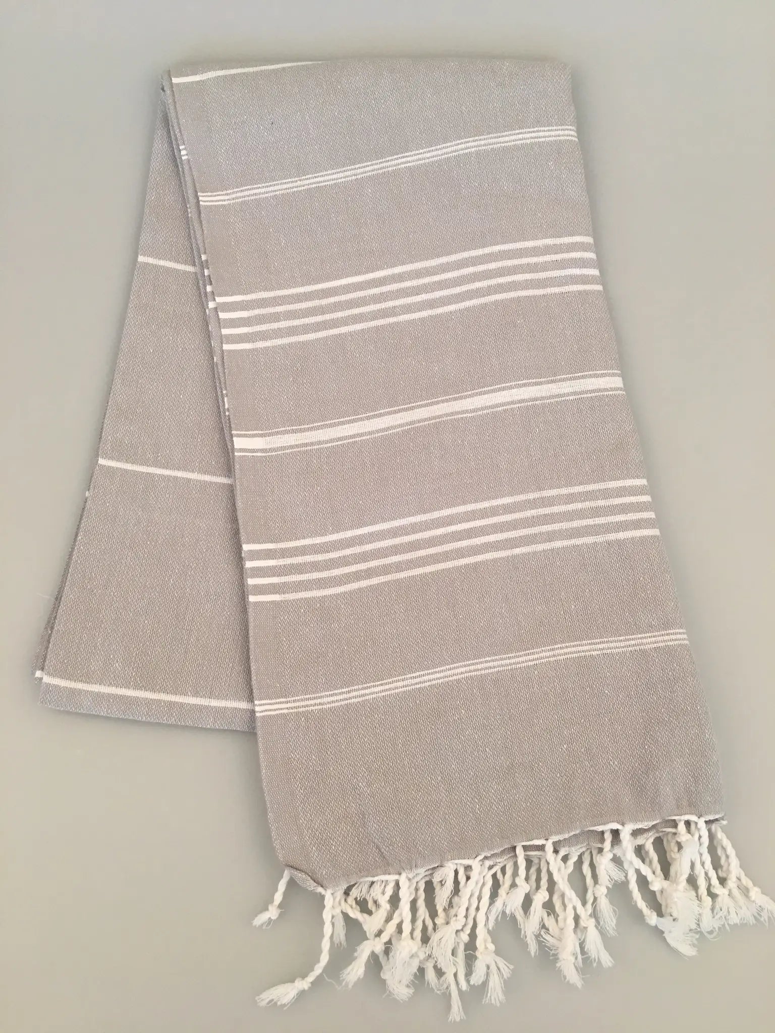 Light gray Turkish towel with white stripes and fringed edges, folded on a neutral background.