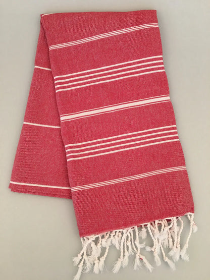 "Red Turkish towel with white stripes and fringed edges, folded neatly, textured fabric"