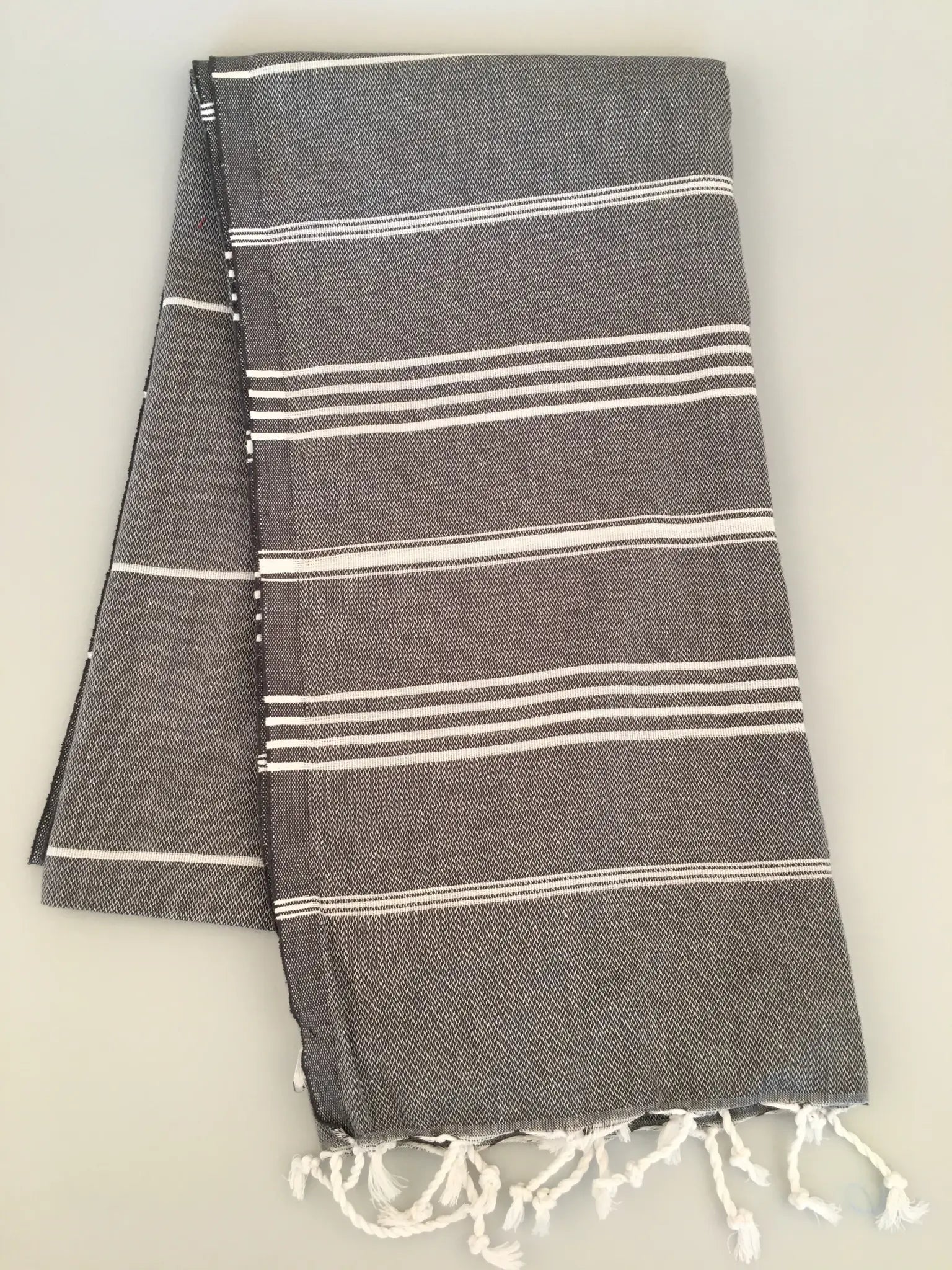"Gray Turkish towel with white stripes and fringed edges, folded neatly on a light background."