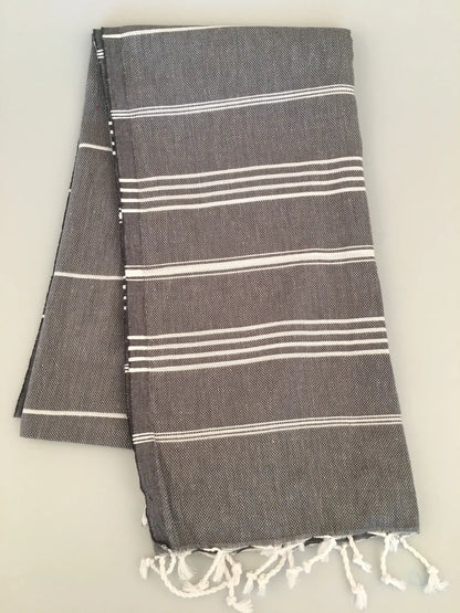 "Gray Turkish towel with white stripes and fringed edges, folded neatly on a light background."
