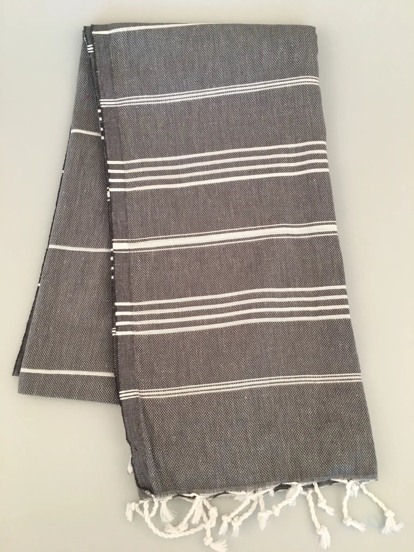 Gray Turkish towel with white stripes and fringed edges, folded neatly, showing soft texture and a lightweight design.
