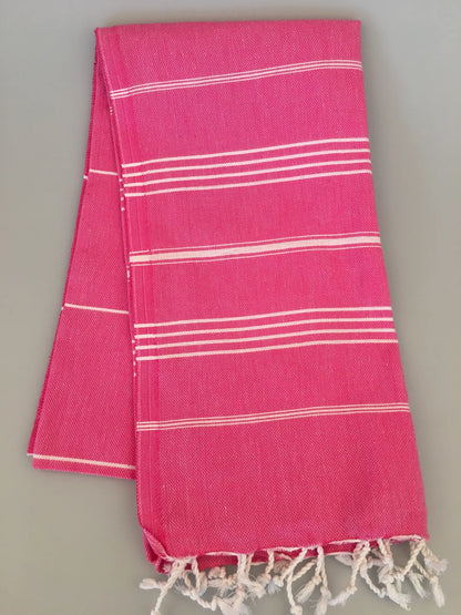 "Bright pink Turkish towel with white stripe patterns and fringed edges, neatly folded."