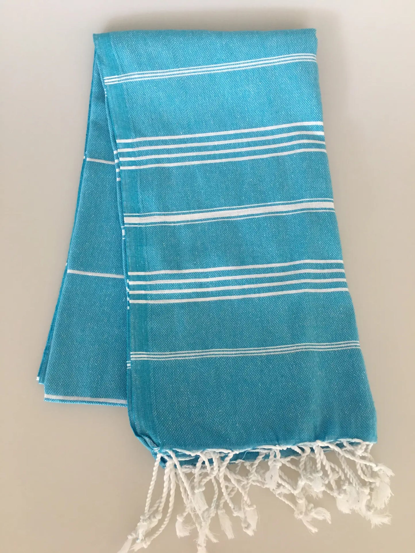 Aphrodisias Sultan Turkish towel peshtemal in vibrant turquoise with white stripes and fringed edges, folded neatly.