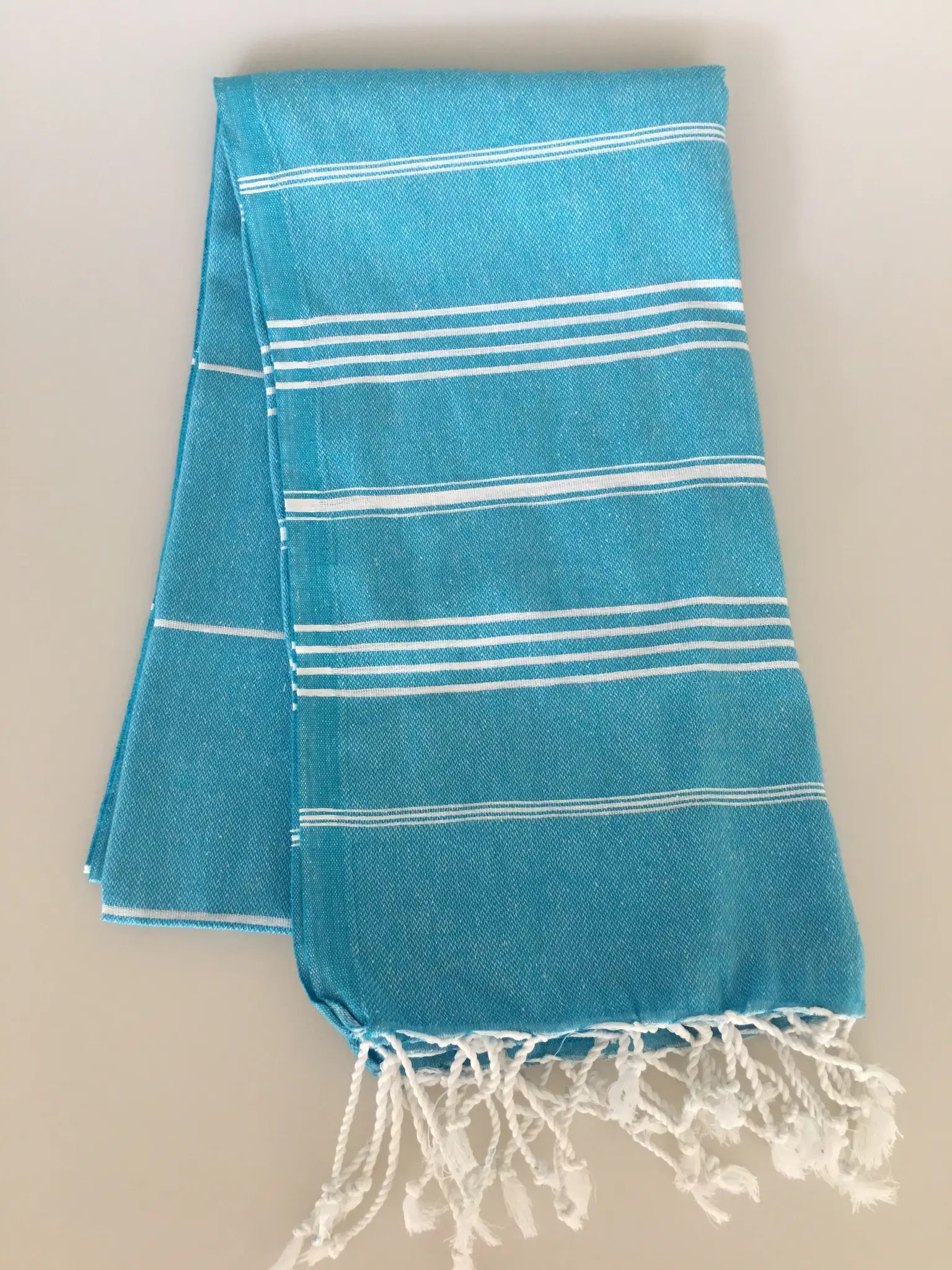 Aphrodisias Sultan Turkish towel in turquoise with white stripes, featuring fringed edges, folded flat on a neutral backgroun