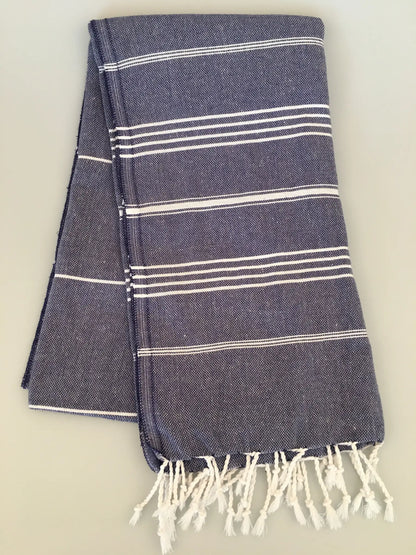 "Dark blue peshtemal towel with white stripes and fringe edges, neatly folded on a light background."