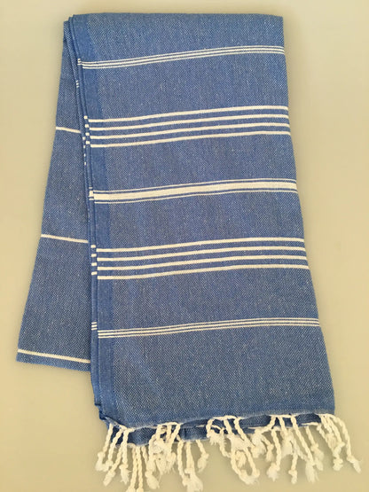 "Blue Turkish towel with white stripes and fringed edges, folded neatly on a light background."