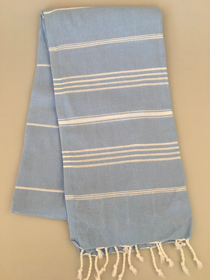 Light blue Turkish towel with white stripes, fringed edges, and a soft, textured weave, laid flat.
