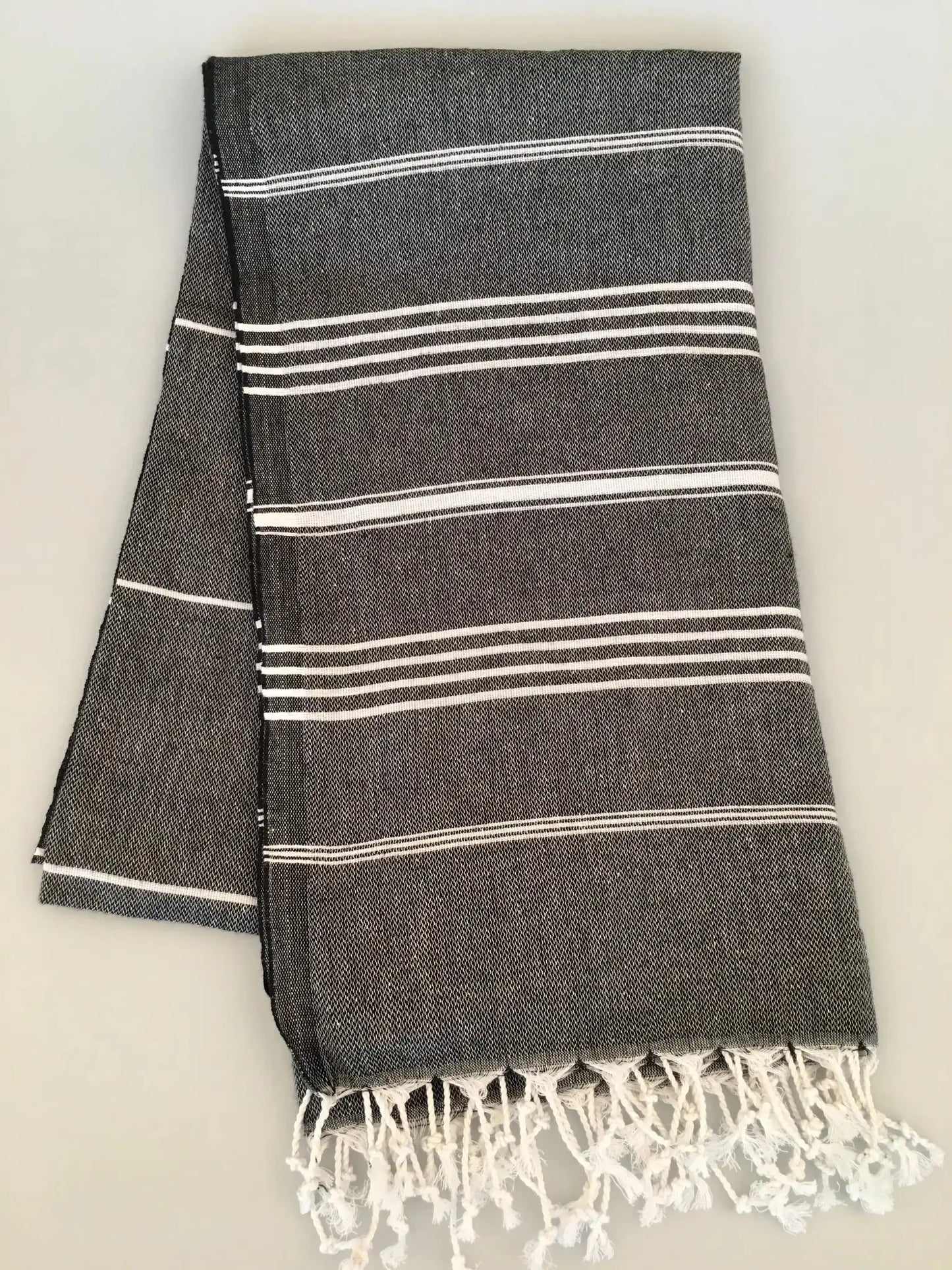 Gray Turkish towel with white stripes and fringed edges, neatly folded on a light background.