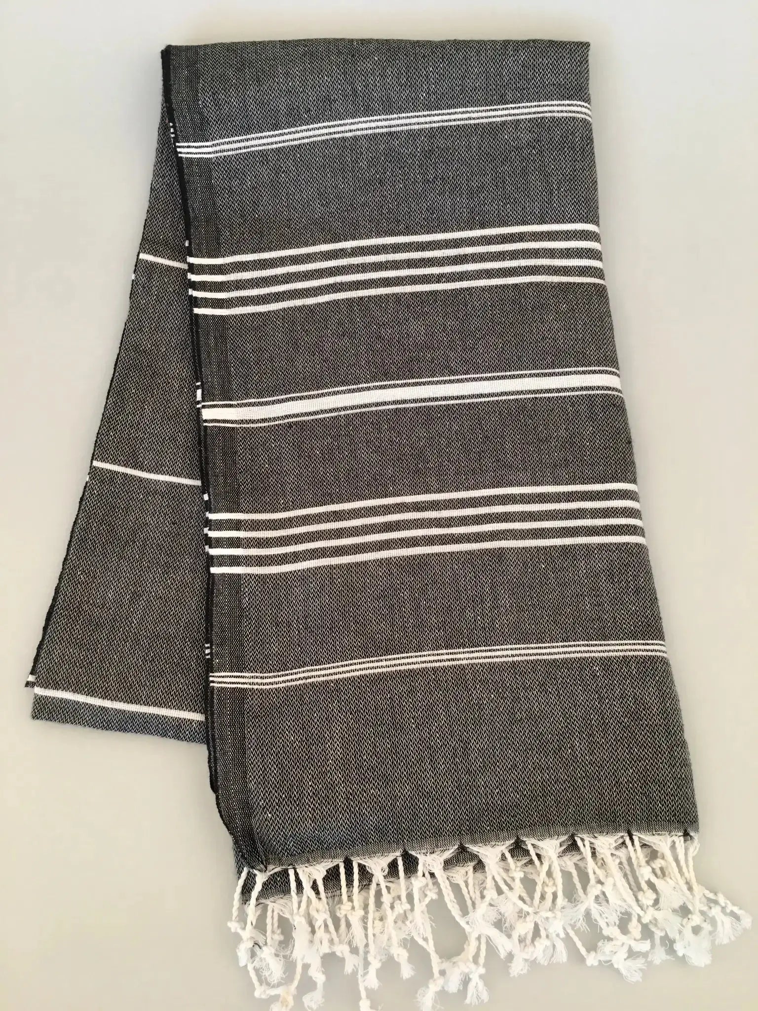 Gray Turkish towel with white stripes and fringed edges, neatly folded on a light background.