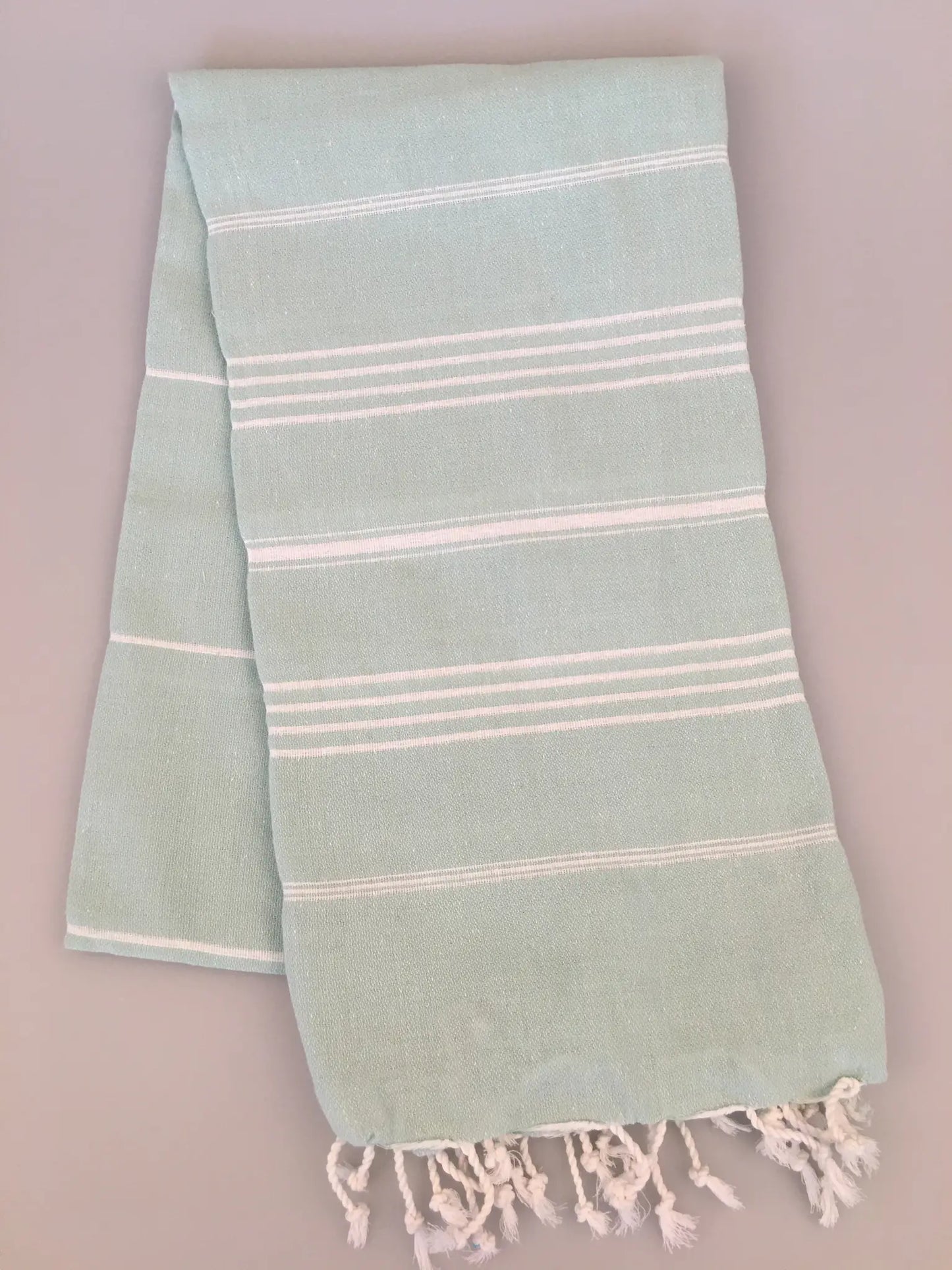 Light blue Turkish towel with white stripes and fringed edges, neatly folded.