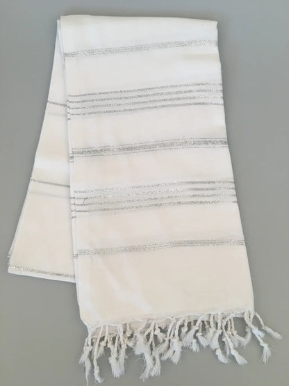 "White Turkish towel with silver striped patterns and fringed edges, laid flat on a light gray background."