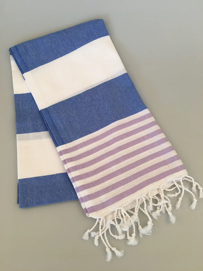 "Tralles Turkish towel peshtemal in blue and white stripes with purple stripes, featuring white fringes on one edge."