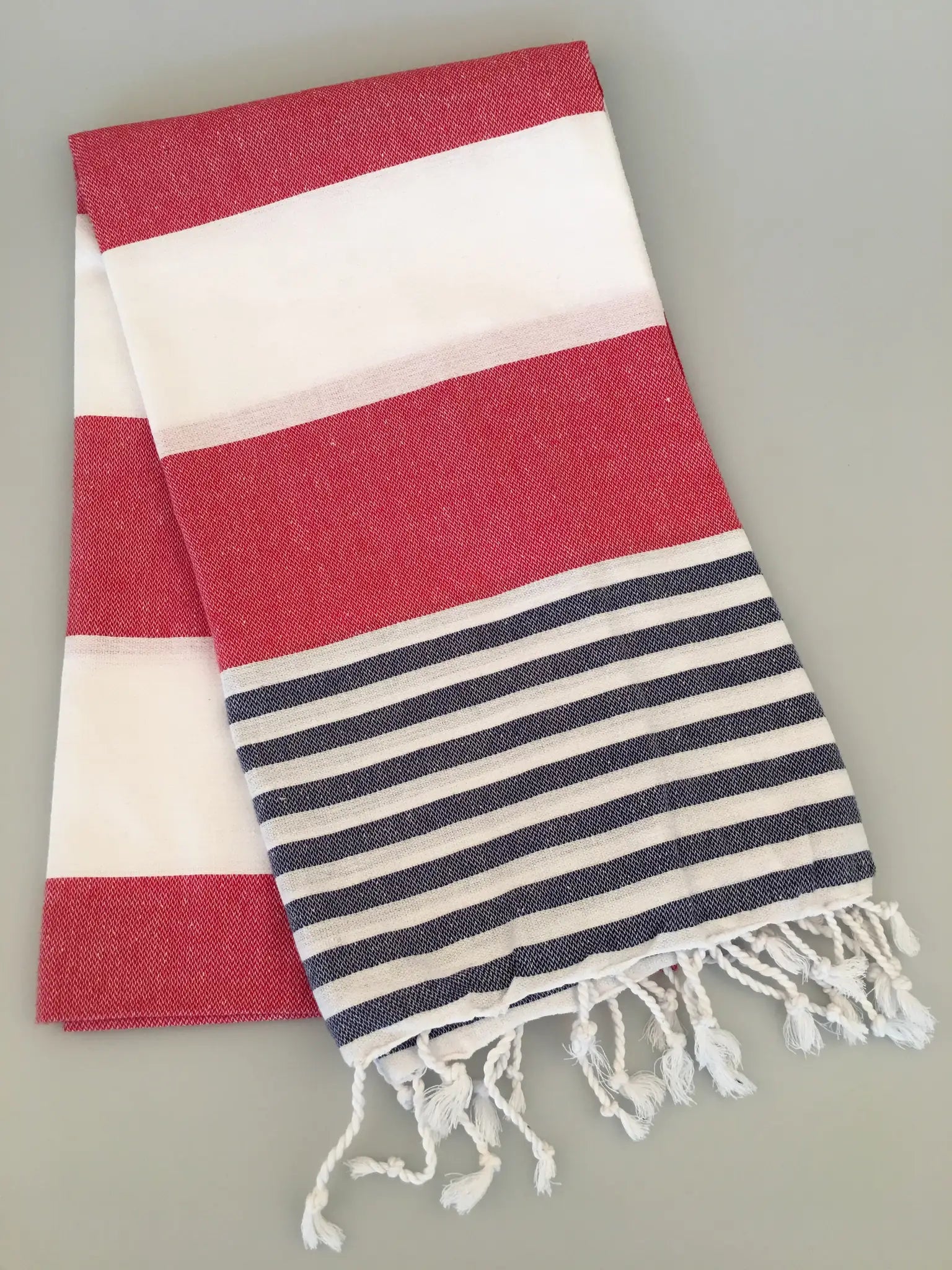 "Red and white striped Turkish towel with navy blue stripes at the bottom and fringed edges, laid flat."