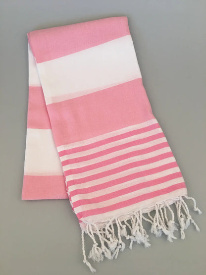 "Pink and white striped Turkish towel with fringed edges, folded on a light gray background."