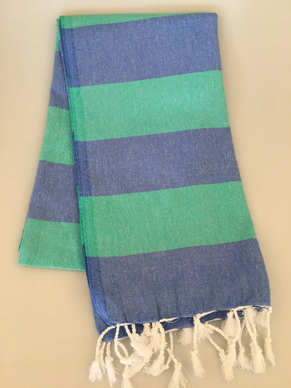 "Blue and green striped Turkish towel with fringed edges, folded neatly on a light background."