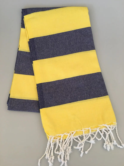 "Yellow and navy striped Turkish towel with white fringes, laid flat on a light gray surface."