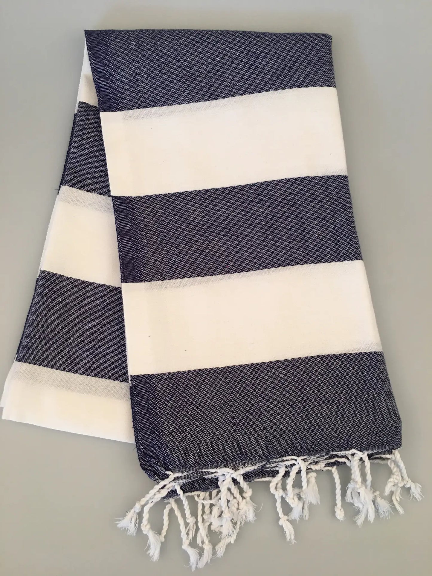 "Navy blue and white striped Turkish towel with fringed edges, folded on a light gray surface."