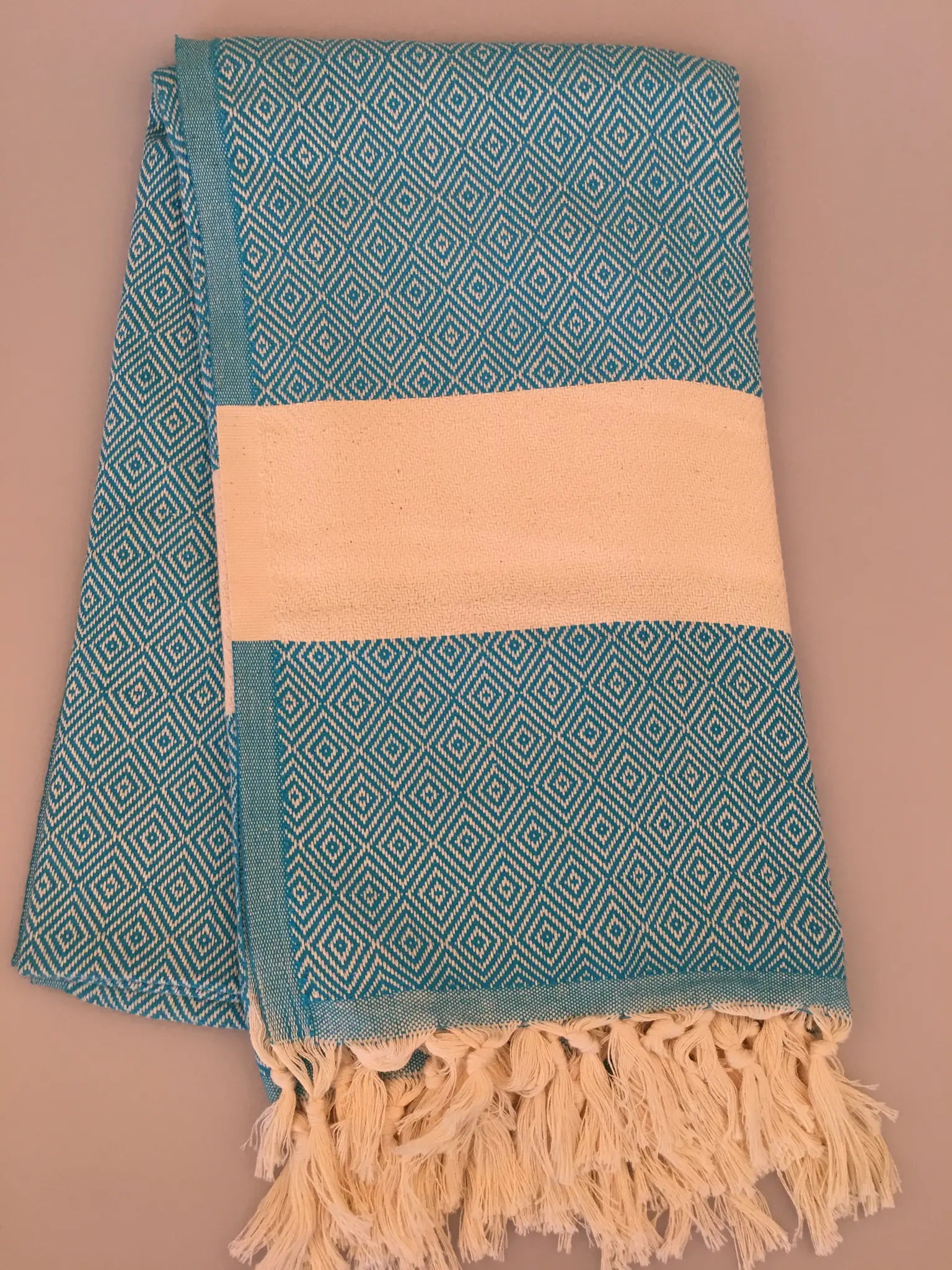 Turquoise and white Turkish towel with diamond pattern and fringed edges, folded neatly on a neutral background.