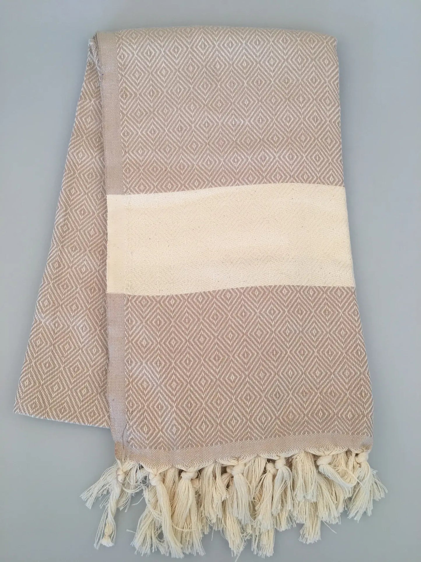 "Beige Turkish towel with diamond pattern, cream stripe, and fringed edges, laid flat on a light background."