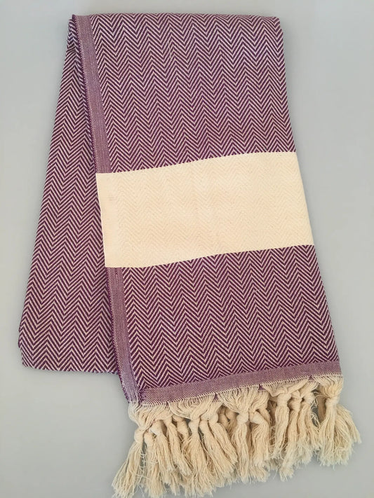 "Purple and white herringbone-patterned Turkish towel with fringed edges, laid flat on a light background."