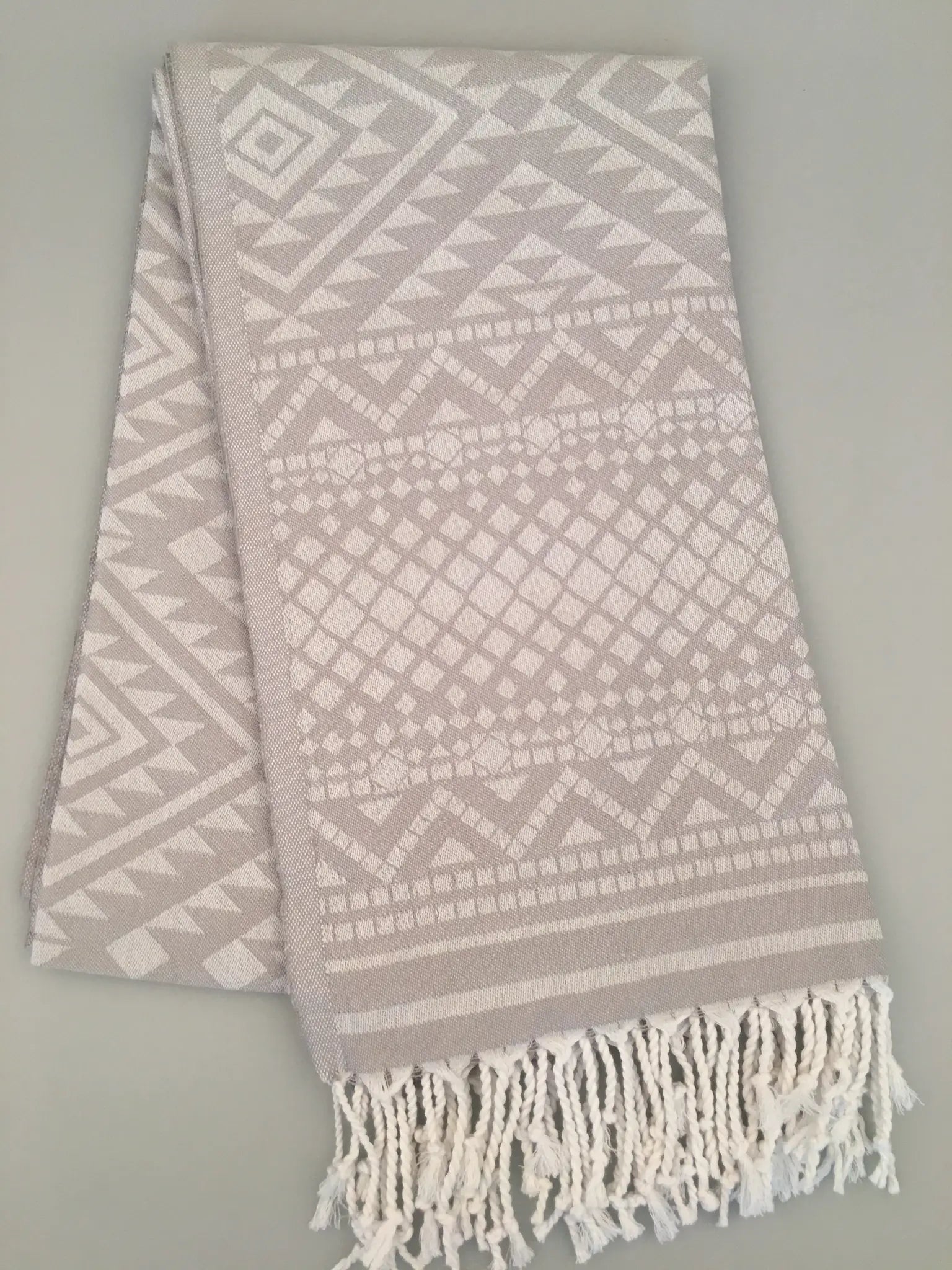 "Light gray Turkish towel with jacquard patterns in white, featuring fringed edges, folded view."