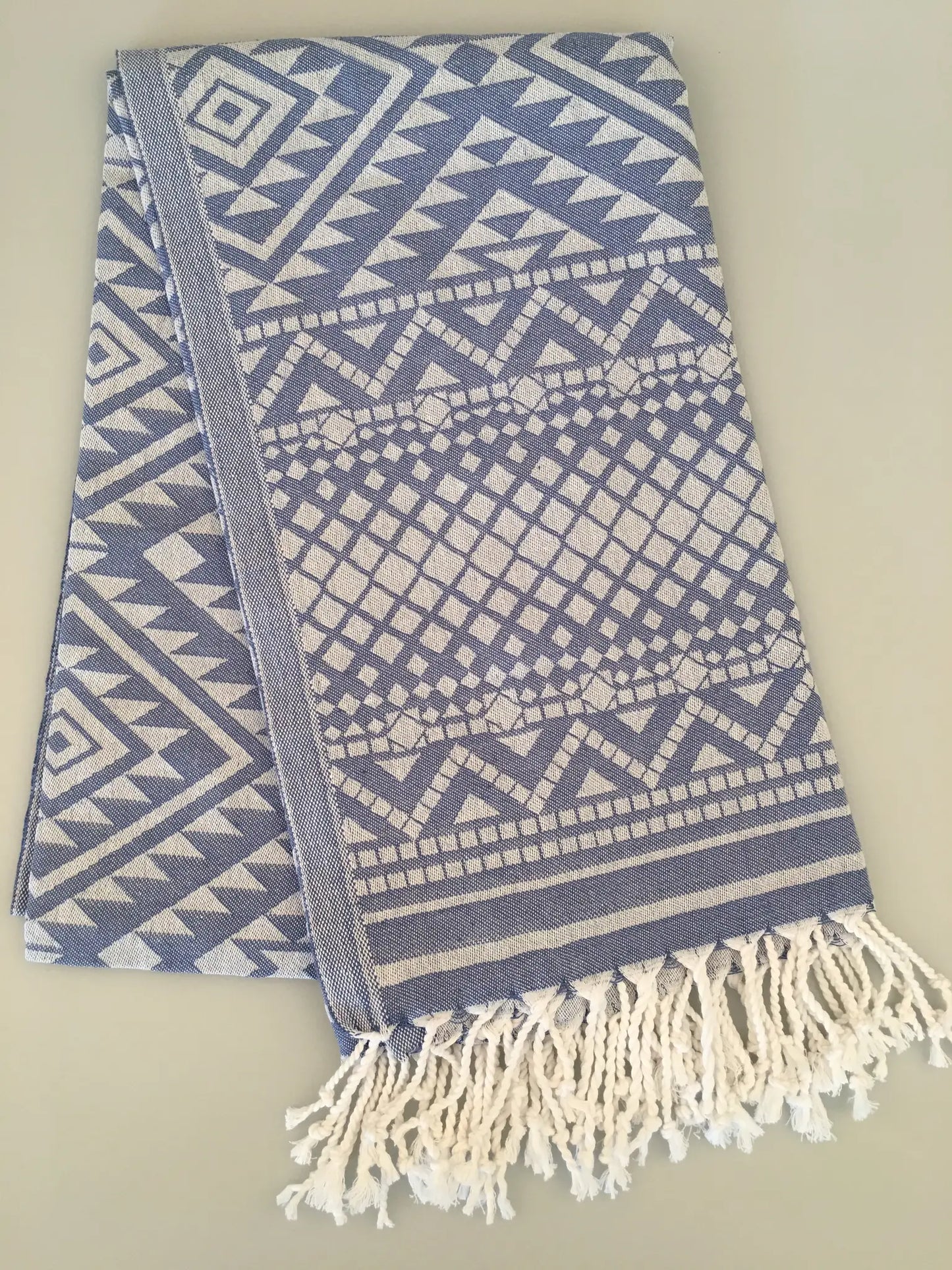 "Blue and white jacquard peshtemal towel with geometric patterns and fringed edges, folded on a light background."
