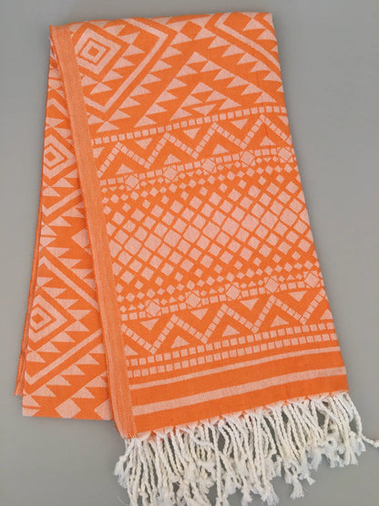 Orange Turkish towel with white jacquard patterns featuring geometric shapes, finished with white fringes at one end.