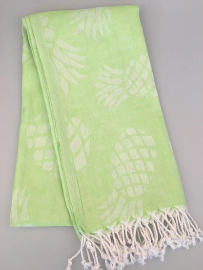 Light green Turkish towel with white pineapple jacquard pattern and fringed edges, folded view on a gray background.