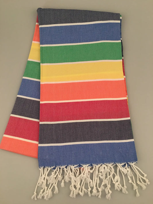 Colorful Iasos Turkish Towel Beach Peshtemal with horizontal stripes in blue, green, yellow, red, and orange, fringed edges.