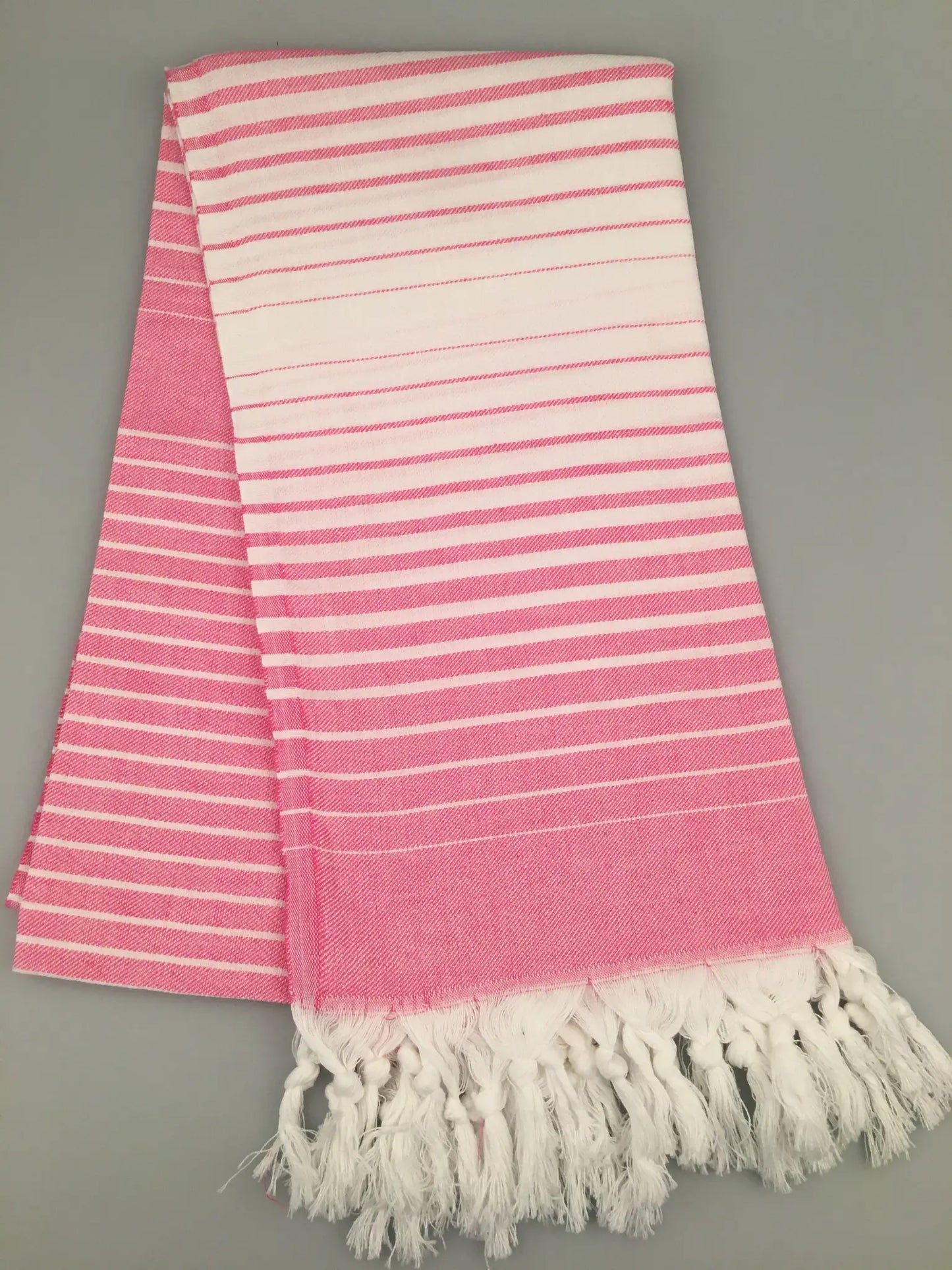 "Telmessos Turkish Towel Peshtemal in pink and white stripes with fringed edges, laid flat on a gray background."