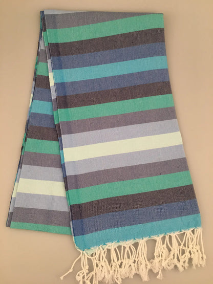 "Turquoise, blue, and gray striped Turkish towel with fringed edges, folded on a light background."