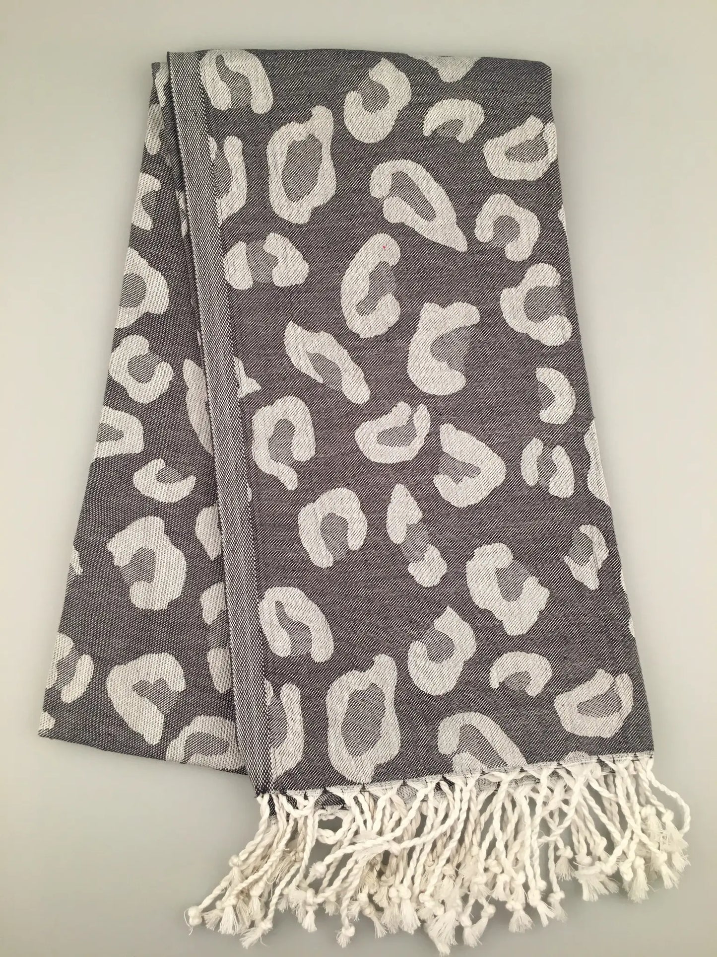 Gray Turkish towel with white leopard print pattern, fringed edges, folded flat on a light background.