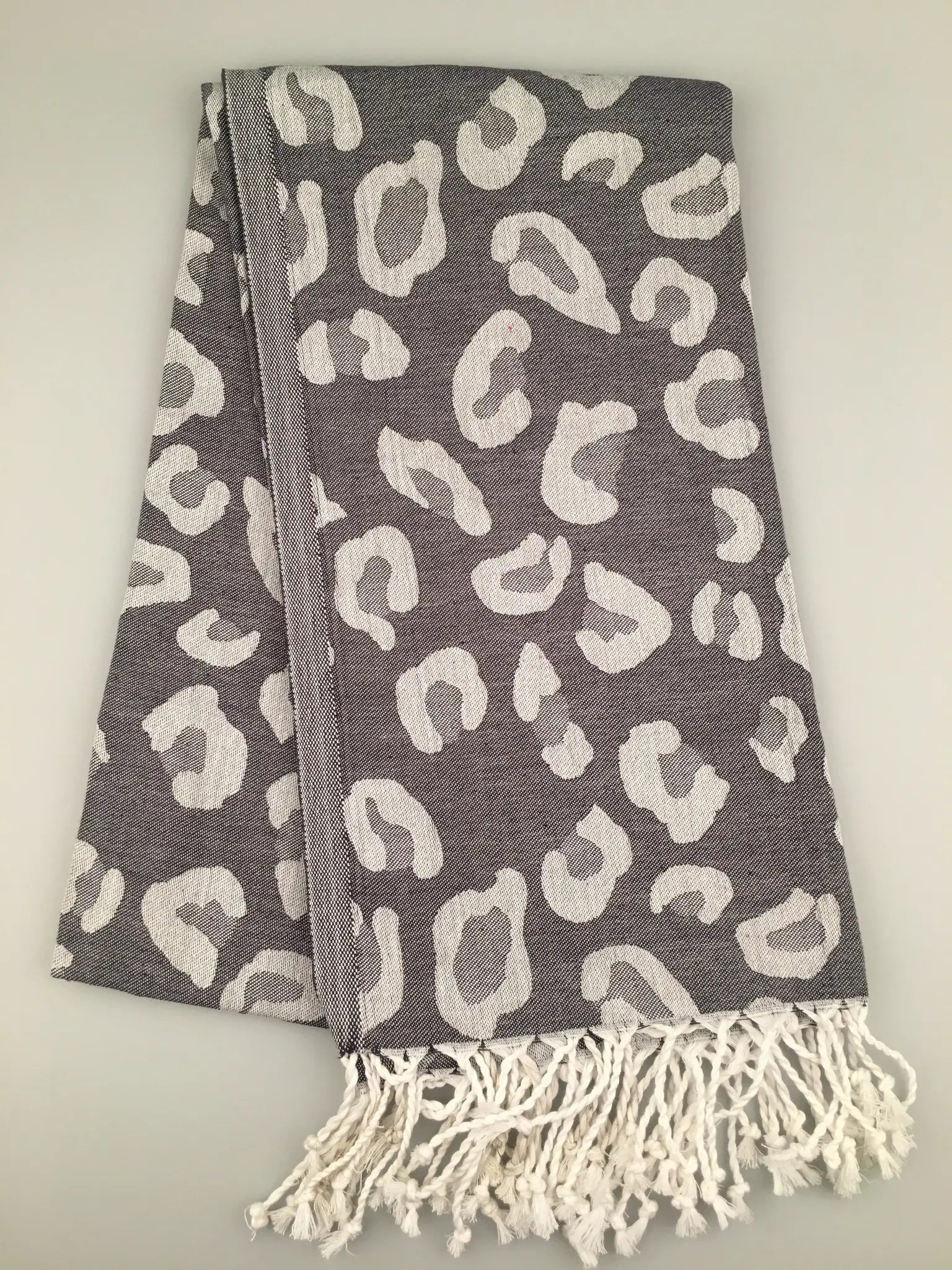 Gray Turkish towel with white leopard print pattern, fringed edges, folded flat on a light background.