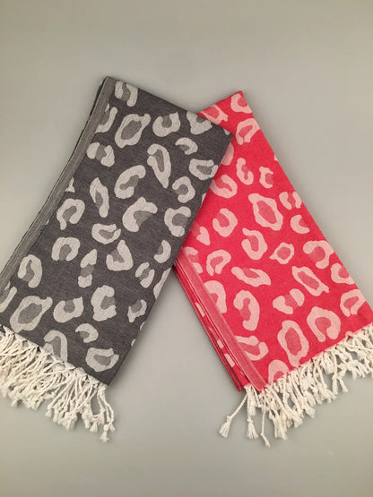 "Gray and coral Turkish towels with leopard print pattern and fringed edges, laid flat on a light background."