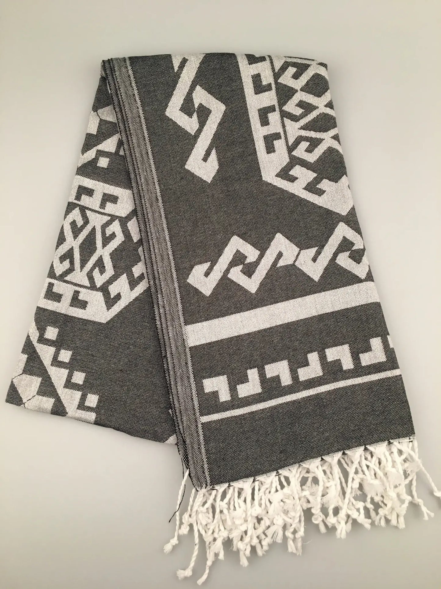"Gray Turkish towel with white geometric jacquard patterns and fringed edges, laid flat on a light background."
