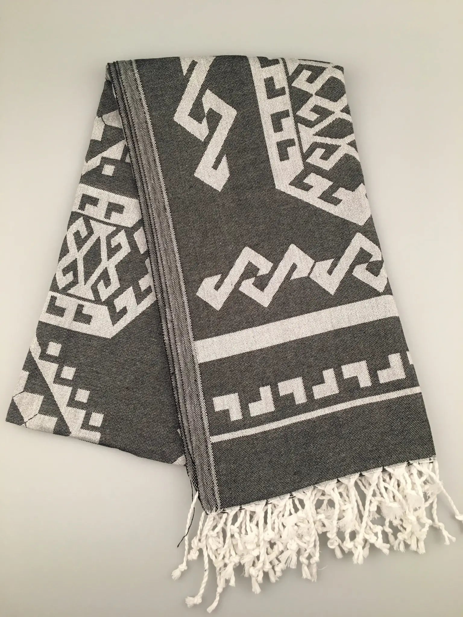 "Gray Turkish towel with white geometric jacquard patterns and fringed edges, laid flat on a light background."