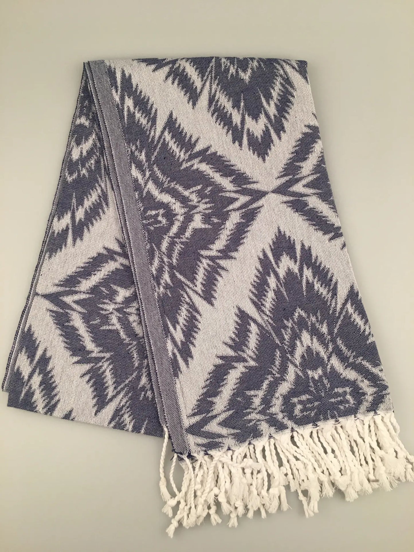 "Gray and navy jacquard Turkish towel with a geometric pattern and white fringes, laid flat on a light background."