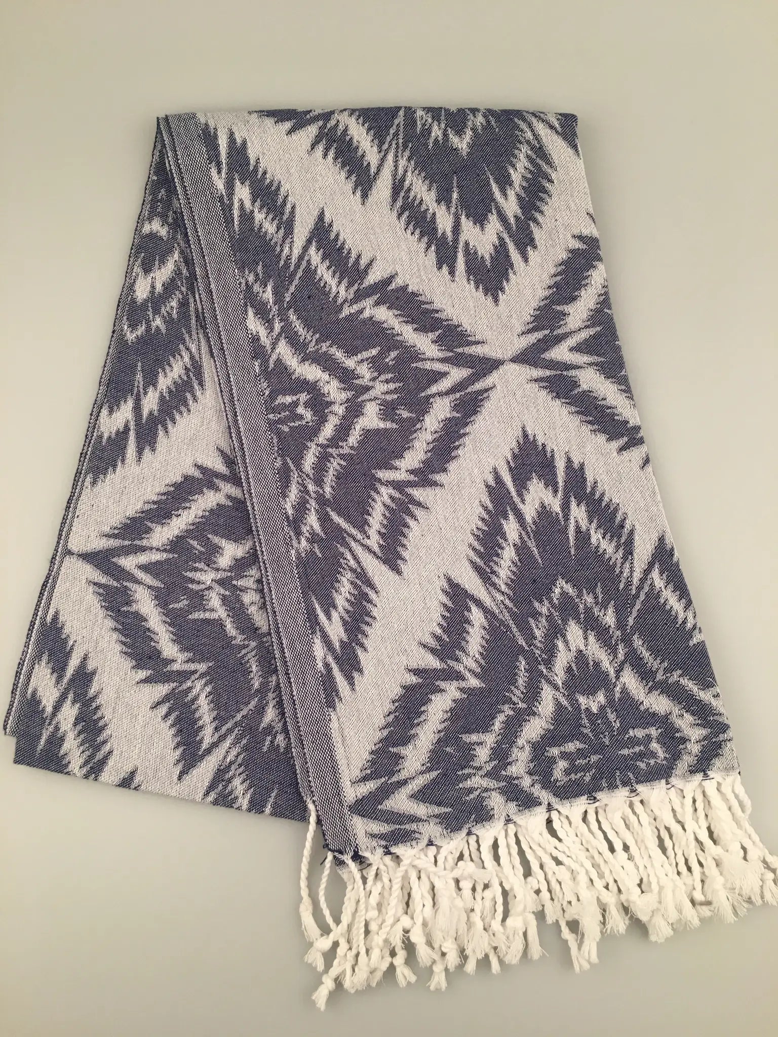 "Gray and navy jacquard Turkish towel with a geometric pattern and white fringes, laid flat on a light background."