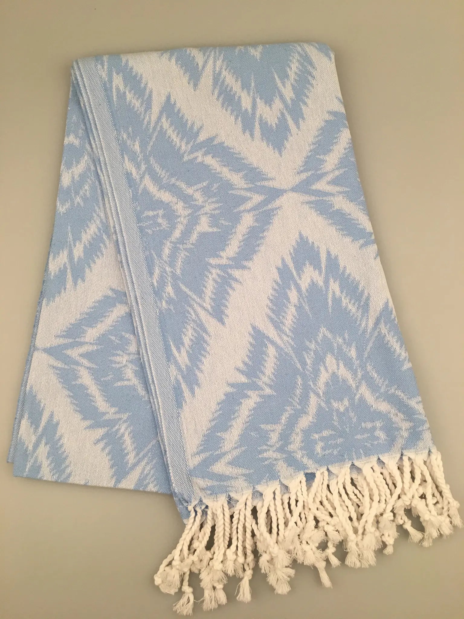 "Light blue Jacquard Turkish towel with white geometric pattern and fringed edges, displayed on a neutral background."