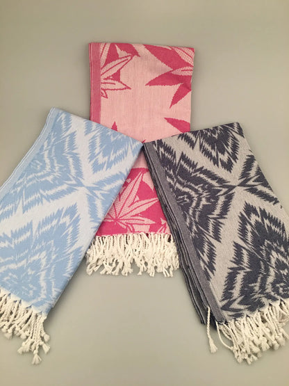 "Three Larisa Turkish towels: pink with leaf pattern, light blue geometric design, and gray with similar pattern, each with f